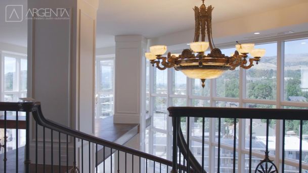 An elegant chandelier with glowing lights hanging over a modern staircase with large windows.