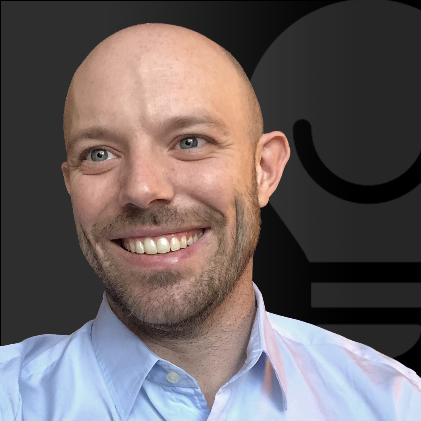 Smiling man with light stubble wearing a light blue button-down shirt, posed in front of a dark background featuring a large, abstract lightbulb icon.