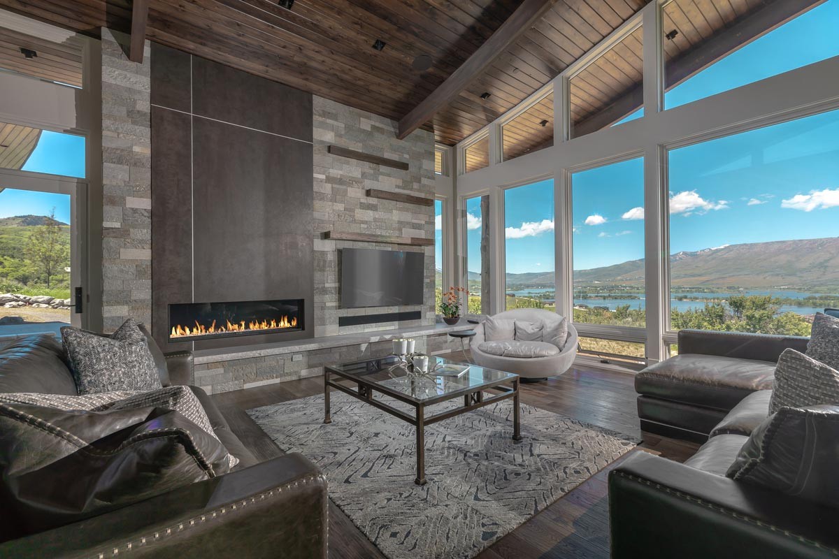 A large media room with a TV, soundbar, overhead speakers, several couches, and a beautiful view of mountains through floor-to-ceiling windows. 