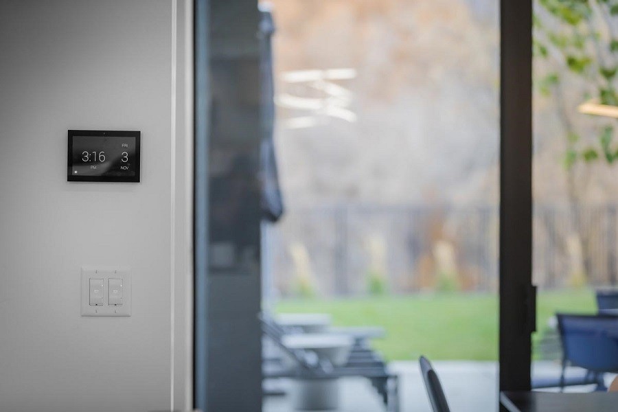A sophisticated Control4 touchpanel mounted on the wall next to a sliding glass door overlooking a backyard.