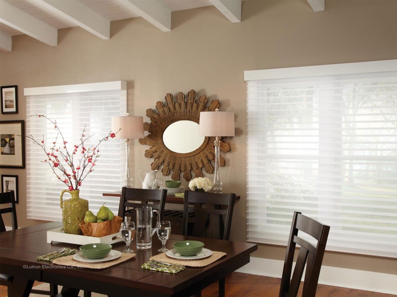 A dining table set with plates and silverware with large windows featuring motorized blinds on both sides. 