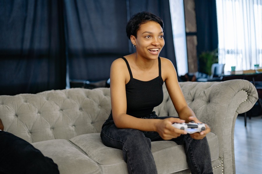 Woman smiles while playing gaming console, sitting on the couch.