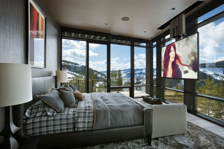 A bedroom with picture windows overlooking the mountains and an in-ceiling TV and speakers.