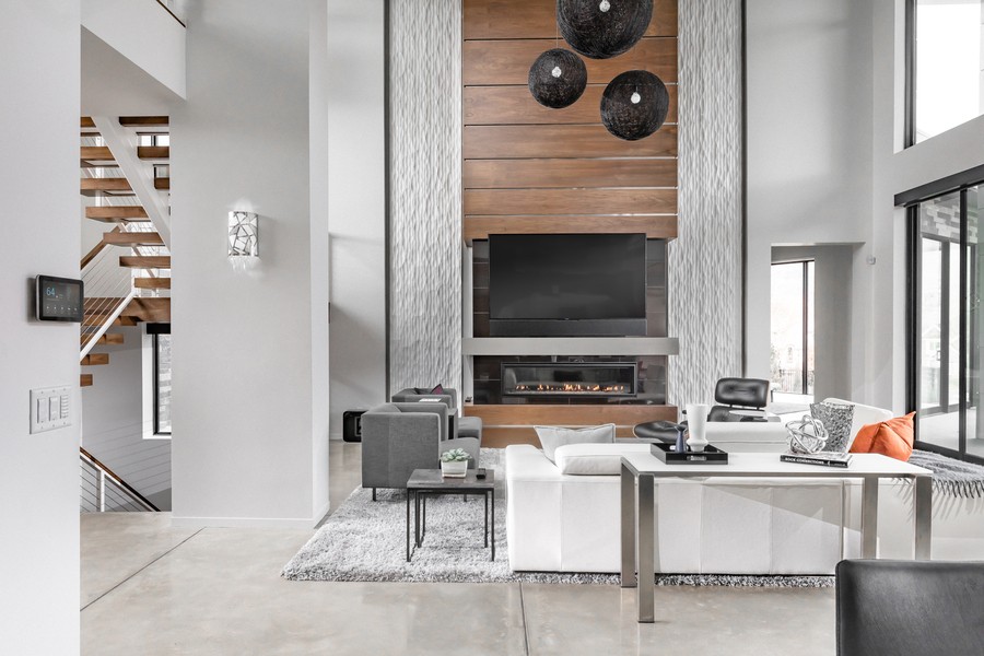 Modern luxury living room with tall ceilings, a wall-mounted TV above a linear fireplace, neutral furniture, and large windows for natural light.