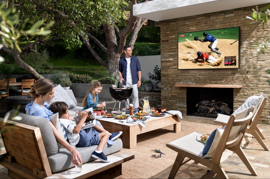 Samsung's The Terrace outdoor TV is mounted on an elegant patio setting above a stone fireplace. 