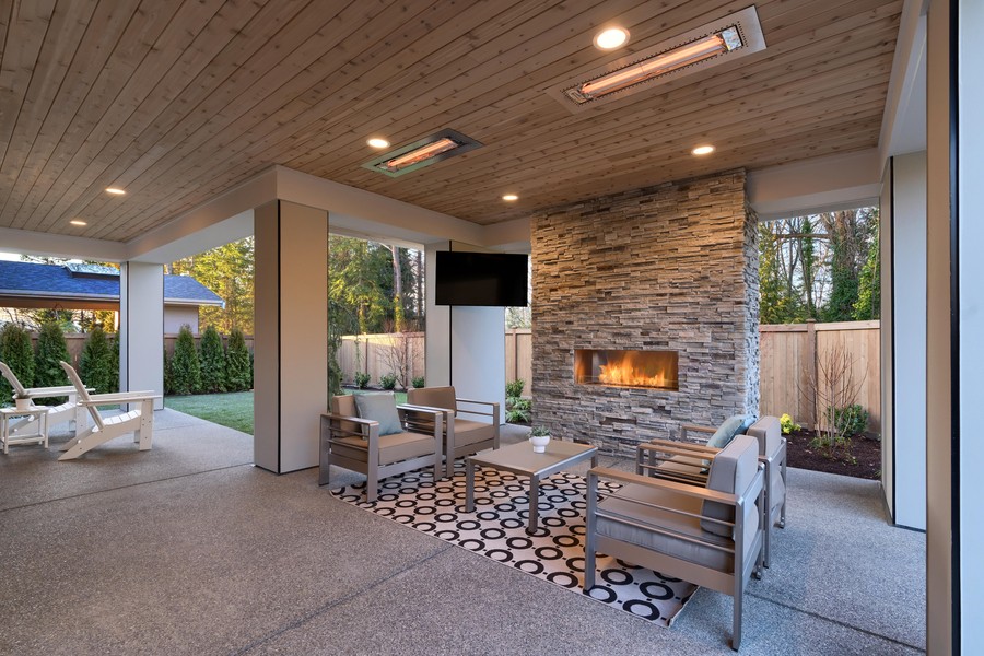 A patio with a fireplace, TV, seating, and infrared, in-ceiling heaters. 