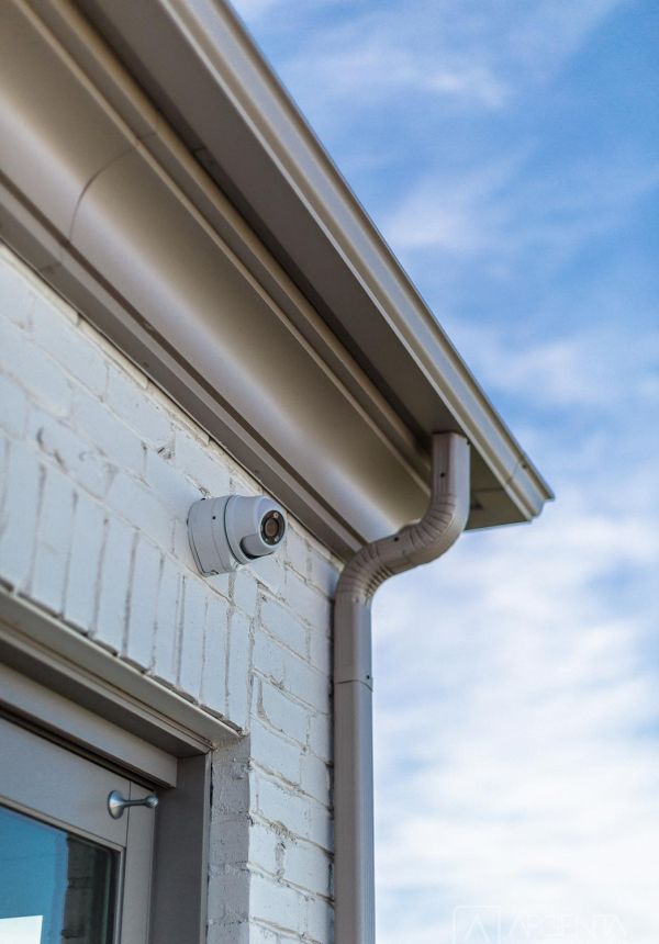 Outdoor security camera installed on white brick exterior under roof gutter