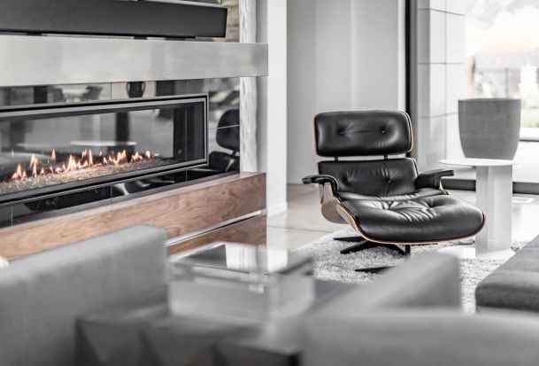 Modern living room with a sleek linear fireplace, black leather lounge chair, and minimalist decor.