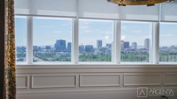 A close-up of large glass windows with a bright reflection of the chandelier and surrounding city skyline.