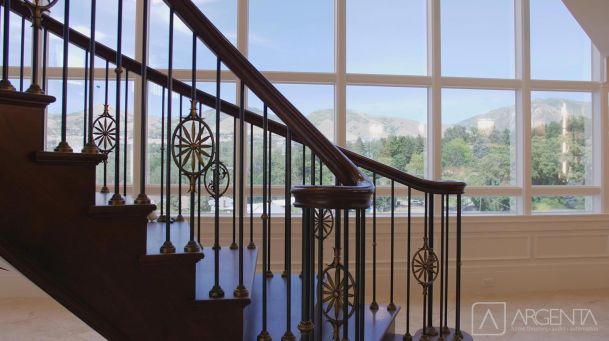 A beautifully crafted wooden staircase with decorative metal railings, set against large glass windows showing a scenic mountain view.