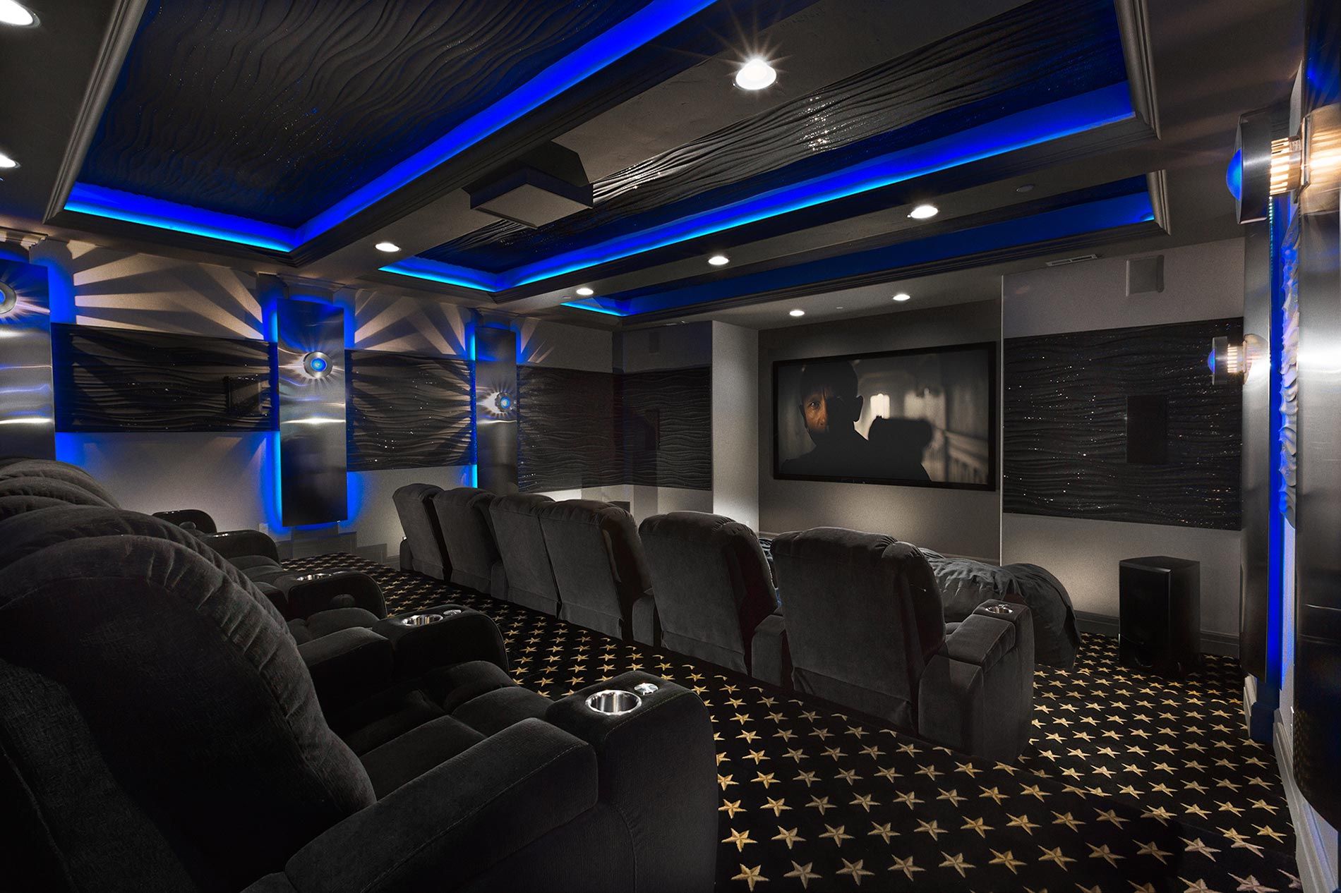 A luxurious home theater featuring comfortable reclining seats, a large screen, and vibrant blue accent lighting.