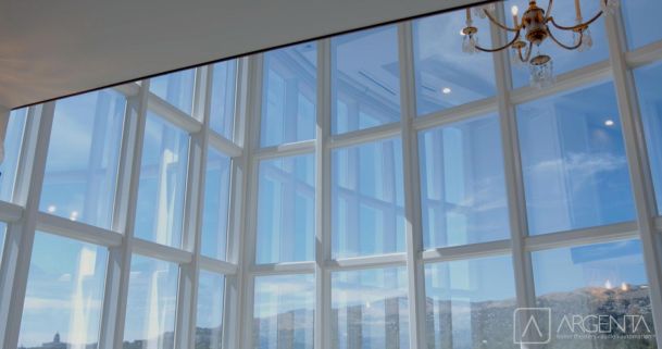 A grand multi-pane glass window with a stunning view of mountains under a clear blue sky.