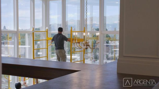 A worker assembling scaffolding in front of tall glass windows that offer a view of rolling hills.